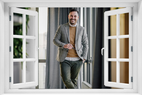 Portrait of smiling confident businessman standing with hand in pocket at office