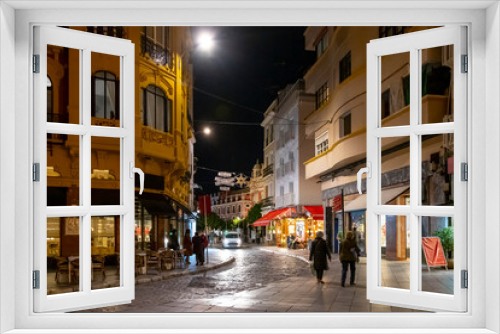Fototapeta Naklejka Na Ścianę Okno 3D - Evening in the Barrio Santa Cruz district in the historical center of the Andalusian city of Seville, Spain, as pedestrians walk the streets among illuminated cafes and shops.