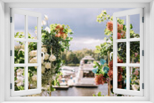 Fototapeta Naklejka Na Ścianę Okno 3D - Arch design for the wedding ceremony is decorated with flower arrangements and stands on the lake background and Yacht Club