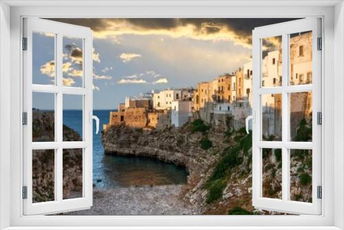 Fototapeta Naklejka Na Ścianę Okno 3D - Polignano a mare, Puglia, Italy. August 2021. Amazing aerial view of Cala Monachile: the picturesque and fascinating beach of the historic center. At sunset, the golden hour, people enjoy the place.
