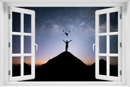 Fototapeta Naklejka Na Ścianę Okno 3D - Young woman traveler standing alone on top of mountain and raise both arms praying and free bird enjoying nature on beautiful night sky, star, milky way background. Demonstrates hope and freedom.
