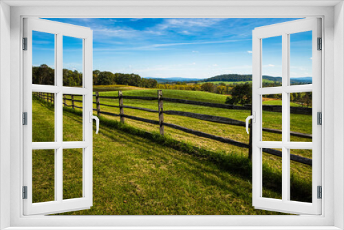 Fototapeta Naklejka Na Ścianę Okno 3D - Meadow with wooden fence, green grass, hilly landscape and blue sky with white clouds on a beautiful summer day in the Sky Meadows State Park, Virginia, USA.