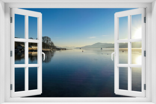 Fototapeta Naklejka Na Ścianę Okno 3D - View on Woerthersee from Poertschach in Carinthia, Austria. Calm lake reflecting the landscape. View on the Karawanks Alps and Pyramidenkogel. Sunset sunrise vibes. Villages at the waters edge. Reed