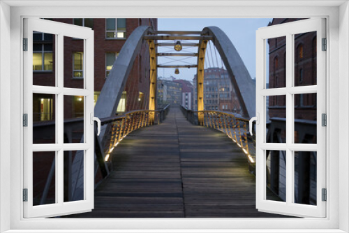 Fototapeta Naklejka Na Ścianę Okno 3D - Metal and wooden industrial pedestrian bridge in the old industrial area of Hamburg in the evening with lights on the metal structure. Hamburg, Germany