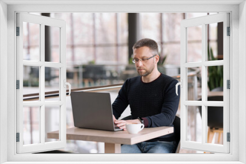 Successful adult man with glasses works on a laptop in a cafe