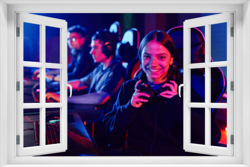 Fototapeta Naklejka Na Ścianę Okno 3D - Portrait of young woman on cyber sports team smiling at camera cheerfully lit by neon light, copy space