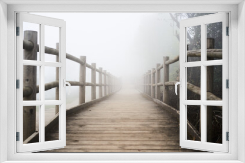 Fototapeta Naklejka Na Ścianę Okno 3D - Winding country road into the mist - Trail, wooden footbridge through dark evergreen forest in fog. Atmospheric autumn landscape. Concepts of ghost, loneliness, silence, gothic, mystery.