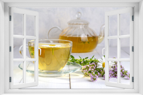 Fototapeta Naklejka Na Ścianę Okno 3D - Herbal tea with chamomile and thyme in a transparent cup on a white wooden table