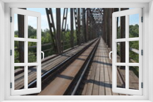 Fototapeta Naklejka Na Ścianę Okno 3D - The metal structure of the railway viaduct over the river against the background of a blue sky with clouds.
