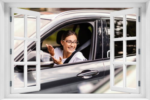 A young woman is sitting in her car in traffic and talking to another driver in the car. She respects traffic regulations. A girl in a car in traffic