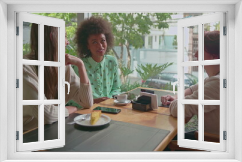 Happy diverse female friends hanging out together at coffee shop. Three young women talking inside cafe smiling and laughing