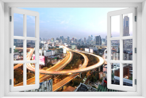 Fototapeta Naklejka Na Ścianę Okno 3D - Panorama of Bangkok at dusk with skyscrapers in background and traffic trails on elevated expressways and circular interchanges ~ Bangkok at rush hour with busy traffic on intertwined highway overpass
