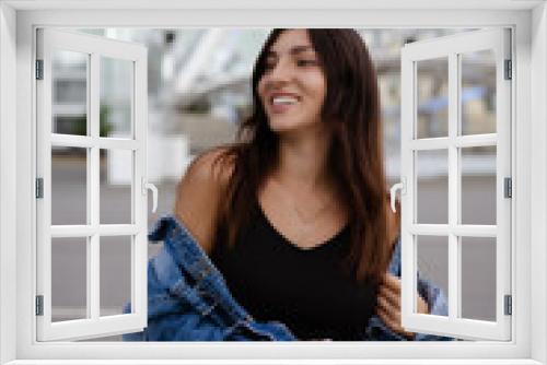 Stylish beautiful young brunette woman model in summer , dressed in a black dress and jeans jacket. Portrait, vertical photo , ferris wheel in the background. Street fashion. Model smiling