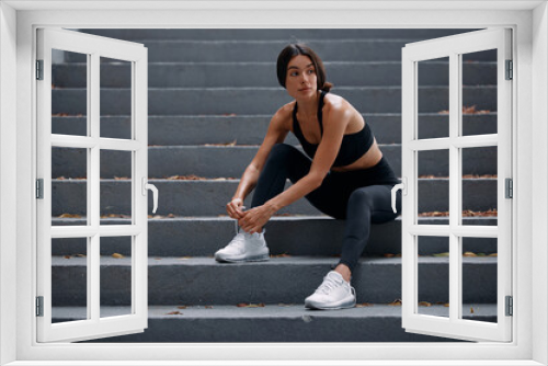 Female runner sitting on the stairs outdoors and tying a shoelace on her sneaker. A runner getting ready for running