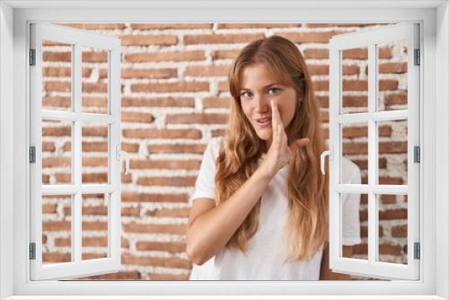 Young caucasian woman standing over bricks wall hand on mouth telling secret rumor, whispering malicious talk conversation