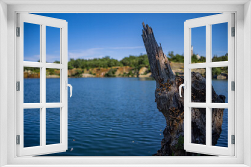 Fototapeta Naklejka Na Ścianę Okno 3D - Broken Sharp Tree Trunk In A Lake With Cliffs In The Background Under Clear Blue Sky, 