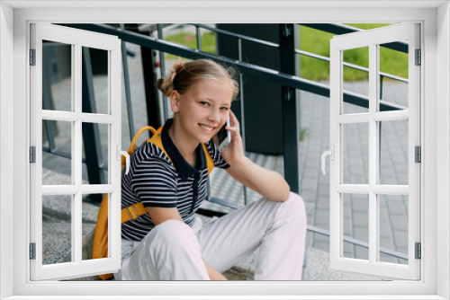 A beautiful girl is sitting on the stairs at school in between classes and talking on the phone