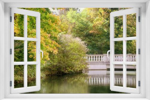 Fototapeta Naklejka Na Ścianę Okno 3D - Beautiful autumnal colors of the tree foliage reflecting of the tranquil waters of a lake crossed by a white stone bridge