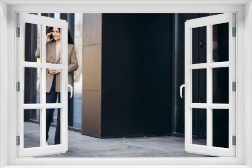 Young business woman walking by the office center using phone and drinking coffee