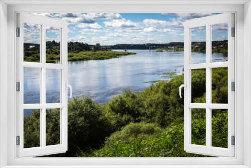Fototapeta Naklejka Na Ścianę Okno 3D - Russia Vologda Oblast Totma 08.12.2017 Summer  landscape: coastline the Sukhona River with blue sky and clouds reflecting in calm water, the village, green trees and grass, and the bridge far away