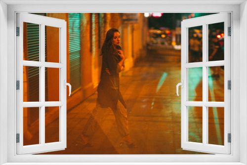 A girl walks around the city at night after the rain among the light of lanterns and cars