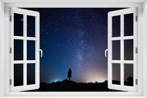 Fototapeta Naklejka Na Ścianę Okno 3D - Milky Way. Night sky with stars and silhouette of a standing happy person with yellow and blue  light. Space background, Astro photography
