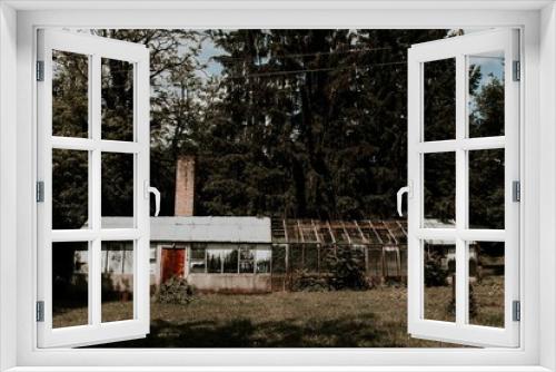 Fototapeta Naklejka Na Ścianę Okno 3D - An abandoned greenhouse by the forest. Broken glasses, rusty metal frames, windows and doors. Ruined building structure, scary looking. 