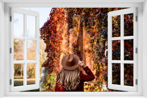 Fototapeta Naklejka Na Ścianę Okno 3D - Young hipster millennials woman in a coat and hat in autumn nature. Model walks in the park and looks at golden autumn, colorful woods, fallen leaves, red loach wall. Autumn walk, people in fall.