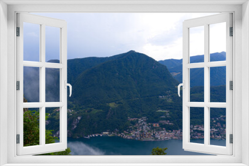 Fototapeta Naklejka Na Ścianę Okno 3D - Aerial view of mountains and lake with Italian Village of Campione seen from local mountain San Salvatore at City of Lugano on a cloudy summer day. Photo taken July 4th, 2022, Lugano, Switzerland.