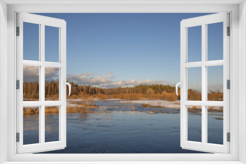 Fototapeta Naklejka Na Ścianę Okno 3D - March sunny evening by the river. Blue sky over the horizon. A picturesque landscape, early spring, a river with snow-covered banks, dry grass and bushes. The first thaws, the snow is melting