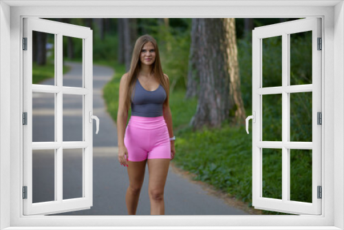 Lovely young woman with sexy boobs in trendy gray top in pink fashionable sports shorts walking on street. Pretty beauty girl fashion model walks in park. Healthy lifestyle.
