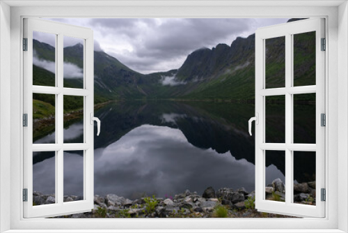 Fototapeta Naklejka Na Ścianę Okno 3D - Wonderful landscapes in Norway. Senja, Nordland. Beautiful scenery of a valley with lupine flowers on the rocks. Mirror in the lake. Cloudy summer day. Fog and mountains in background. Selective focus