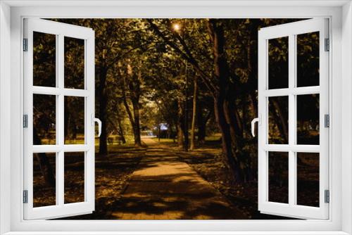Fototapeta Naklejka Na Ścianę Okno 3D - Summer night city park. Wooden benches, street lights, and green trees. The tiled road in the night park with lanterns. Illumination of a park road with lanterns at night. Lutsk
