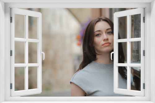 Beautiful Ukrainian girl with red hair, blue eyes and freckles in a grey summer dress leaning with his back against a wall in a cobbled street with street lamps in the old town