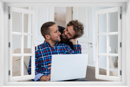 ovely gay couple laughing together while sitting in their living room at home. Two romantic young male lovers having fun surfing the internet indoors. Young gay couple living together.