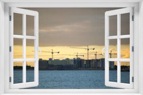Fototapeta Naklejka Na Ścianę Okno 3D - Tower cranes and frame structure of high residential apartment buildings at construction site on sea bay shore. Real estate development at waterfront