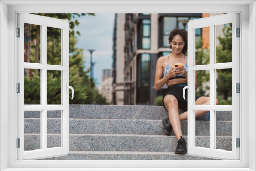 Cute young girl in sportswear sitting on the steps with a phone in hands