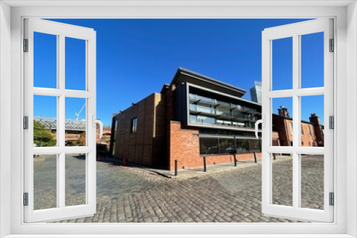 Fototapeta Naklejka Na Ścianę Okno 3D - Modern building on an old cobblestone road with a clear blue sky background. Taken in Manchester England. 