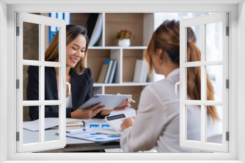 Two young businesswomen pointing to plans, statistics, and data graphs and explaining the conditions of their partnership, happily acknowledging their turnover and income during negotiations.