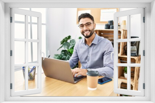 Young arab man smiling confident using laptop and writing on clipboard at office