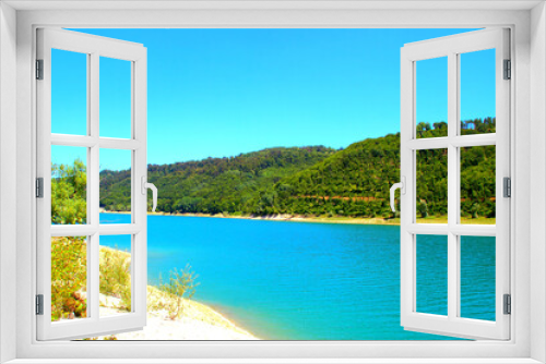 Fototapeta Naklejka Na Ścianę Okno 3D - Clear view of Gerosa Lake with its slightly rippled pristine glowing azure waters sitting between the greenery-topped shores and Marche hills under a cloudless blue sky on a fine summer day
