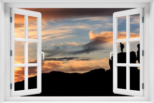 Fototapeta Naklejka Na Ścianę Okno 3D - An orange-pink sunset on the black sea against the background of various black mountains, a small silhouette of a person stands on the mountain. Landscape.
