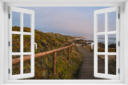 Fototapeta Naklejka Na Ścianę Okno 3D - Wooden walkway with hill with fence and carpobrotus edulis cactus, footpath in seascape at São Paio beach, cliffs and fog on horizon at evening, Labruge PORTUGAL