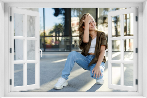 Portrait of teenage girl sitting on floor, urban street, sunlight