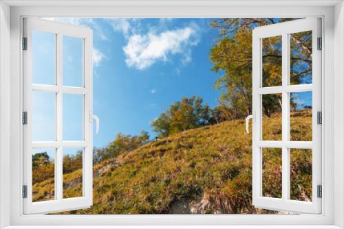 Fototapeta Naklejka Na Ścianę Okno 3D - Mountain landscape with autumn forest in yellow-red foliage. A path on the mountainside on an autumn sunny day. Autumn forest under a cloudy blue sky.