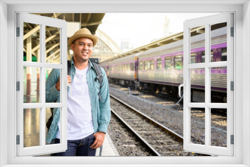 Young asian male traveler backpack in the train station. A man wear a hat and smiling at the railway. Travel concept. The concept of a man traveling alone.