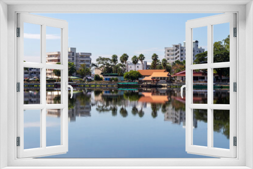 Fototapeta Naklejka Na Ścianę Okno 3D - A view of the pier and bike path for exercise along the shores of the Nong Han River in Sakon Nakhon with reflecting buildings and houses.