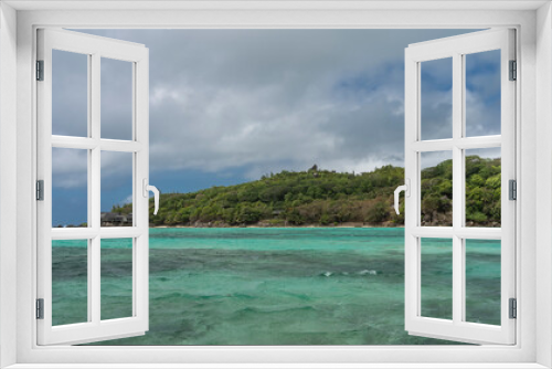 Fototapeta Naklejka Na Ścianę Okno 3D - The island in the turquoise ocean is completely overgrown with tropical vegetation. The villas of the hotel are visible among the trees. Blue sky with clouds. Seychelles