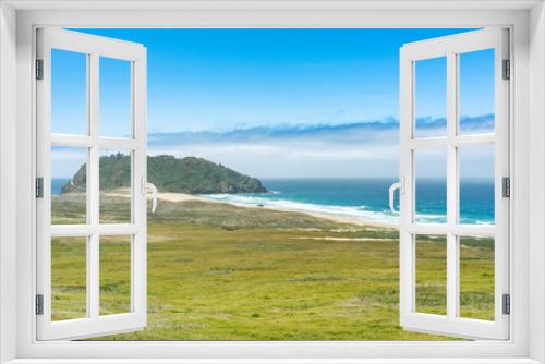 Fototapeta Naklejka Na Ścianę Okno 3D - California, USA - May 19, 2018: grass covered land meeting the sea and a distant island on the pacific ocean under blue sky in big sur