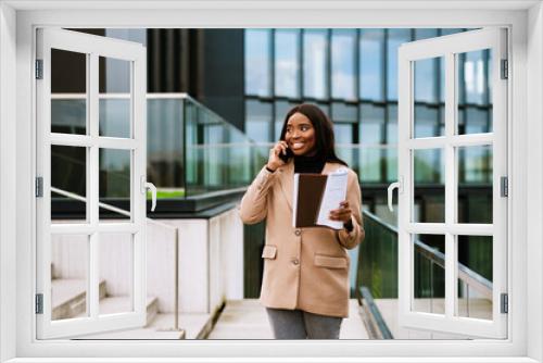 Young black woman talking on cellphone while working with papers